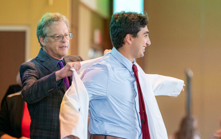 Professor Barry Gidal placing a white coat on a student