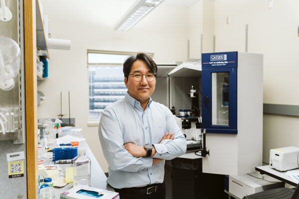 Seungpyo Hong stands with arms crossed in front of lab equipment
