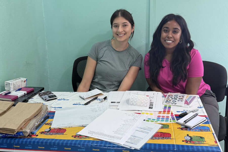 Two PharmD students sit at a table in a rural clinic in Central America. The table is filled with many papers