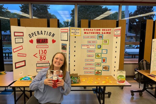 A PharmD student poses in front of a tri-fold about heart health in a school cafeteria