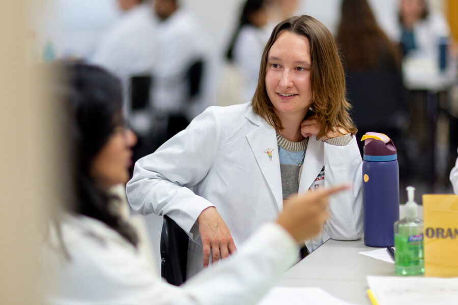 PharmD students in white coats talk to each other during the mental health skills lab