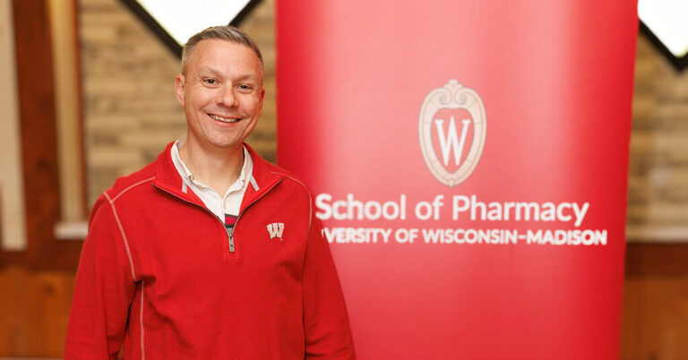 Nick Olson portrait next to a red School of Pharmacy banner