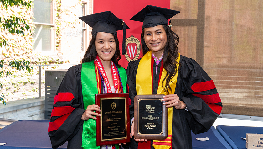 Two smiling PharmD graduates holding award plaques.