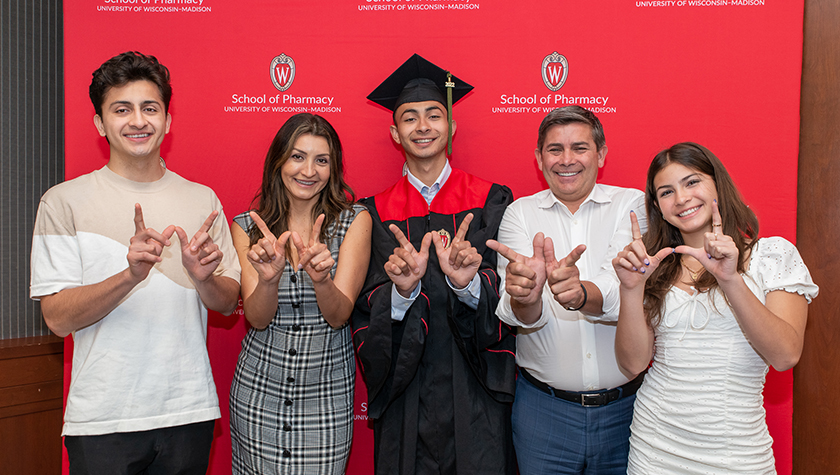 A PharmTox graduate surrounded by family, holding up the "w" for Wisconsin