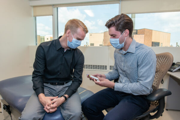 Ryan Simonet and Tyler Albright discuss a medication in a clinic room.