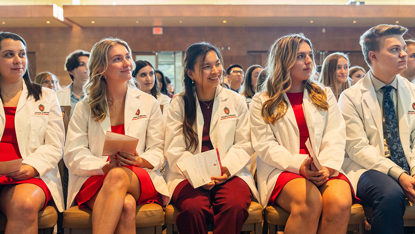 PharmD students sit during the white coat ceremony, smiling at the speaker.