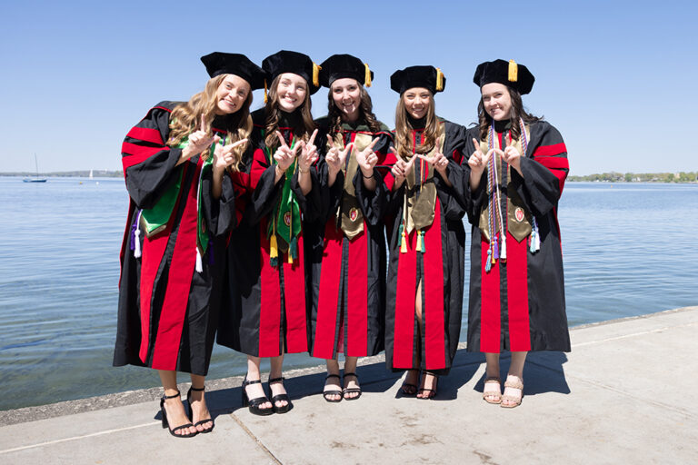 A group of graduates hold up W hands in front of the lake