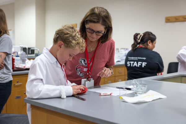 A young boy works at a lab desk with an adult woman looking over his shoulder
