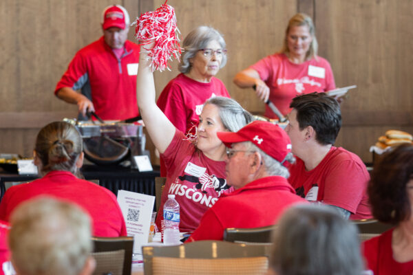 An attendee raising her hand with a pom pom in it, surrounded by other attendees all dressed in Badger red