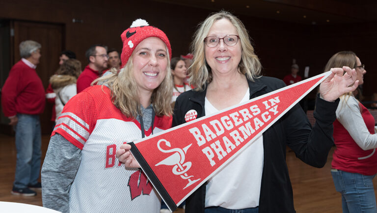 Two School of Pharmacy alumni holding up a Badgers Pharmacy pennant flag.